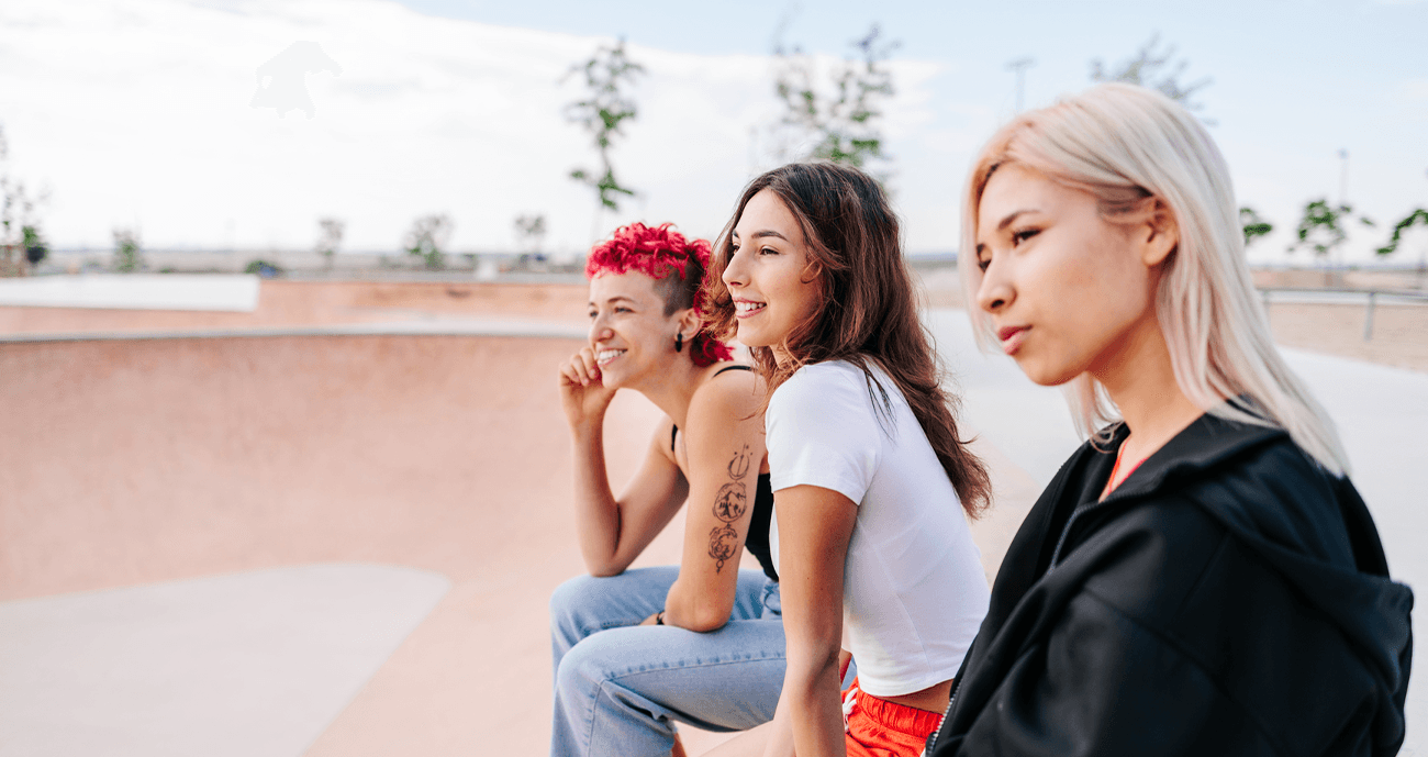 Three women sitting together at a skate park, staring into the distance.